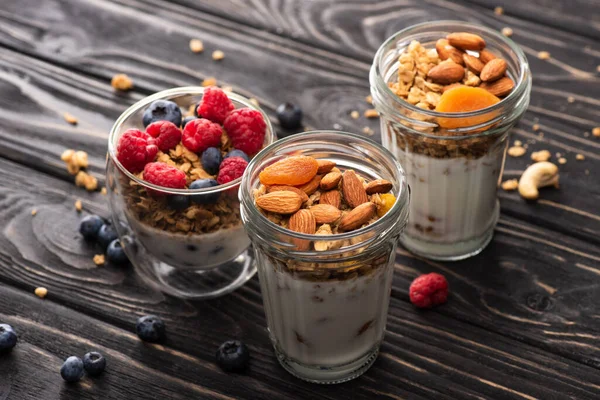 Delicious granola with berries, dried apricots, nuts and yogurt in glass cups on wooden surface — Stock Photo