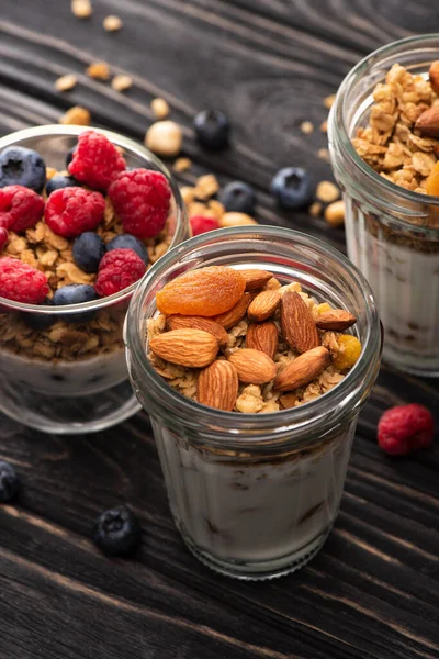 Close-up de granola deliciosa com bagas, damascos secos, nozes e iogurte em copos de vidro na superfície de madeira — Fotografia de Stock