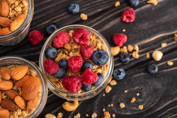 Vista dall'alto di deliziosi muesli con bacche, albicocche secche, noci e yogurt in tazze di vetro su superficie di legno — Foto stock