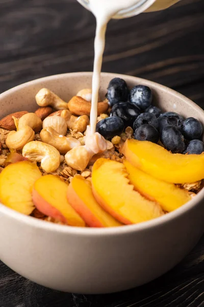 Joghurt auf köstlichem Müsli mit Nüssen, Pfirsich, Blaubeere in Schüssel gießen — Stockfoto