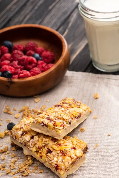 Delicious muesli bars on napkin with blurred glass of milk and berries on background — Stock Photo