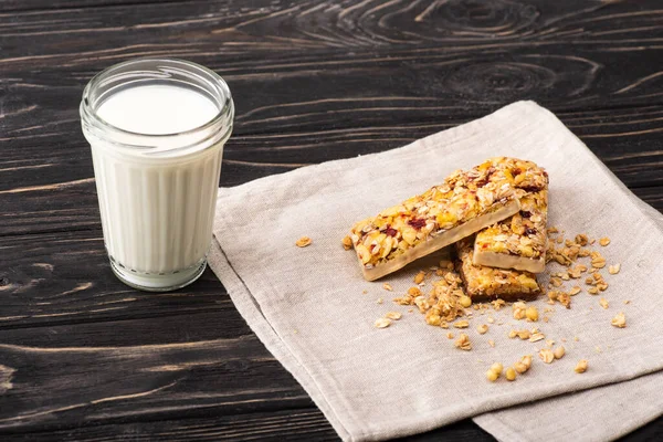 Deliziose barrette di muesli sul tovagliolo vicino a un bicchiere di latte sulla superficie di legno — Foto stock