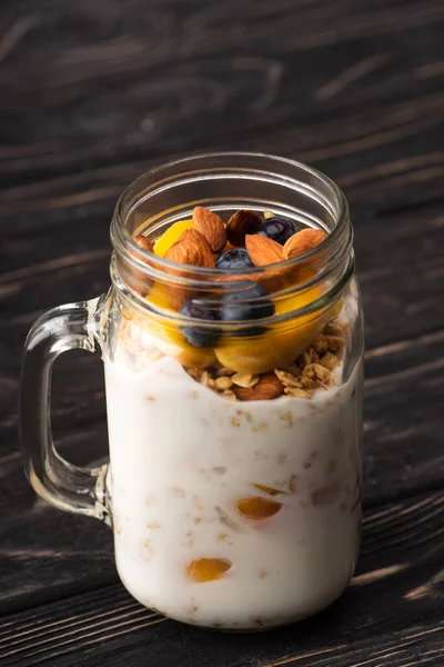Leckeres Müsli mit Joghurt, Nüssen, Pfirsich, Blaubeeren im Glas — Stockfoto