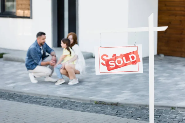 Sign with sold lettering with blurred family squatting near house on background — Stock Photo