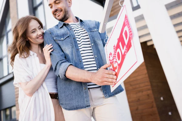 Vue à angle bas du couple souriant tenant signe avec lettrage vendu près de la maison — Photo de stock