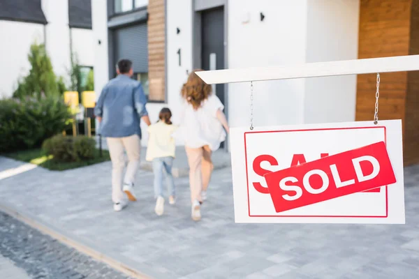 Back view of family going to house near sign with sold lettering on blurred background — Stock Photo