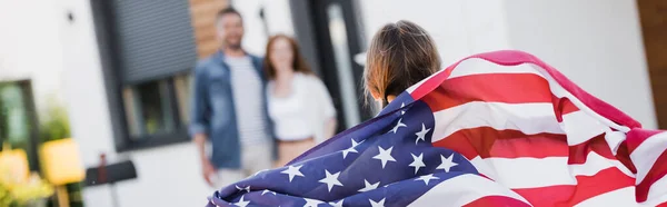 Vista posterior de la hija con bandera americana cerca de los padres borrosos en el fondo, pancarta - foto de stock