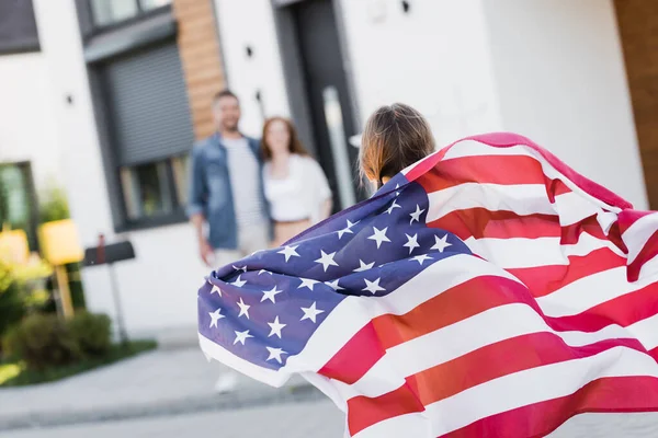 Vue arrière de la fille tenant le drapeau américain avec des parents flous sur le fond — Photo de stock