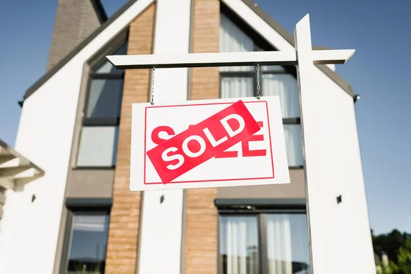 Low angle view of sign with sold lettering with blurred modern house and sky on background — Stock Photo