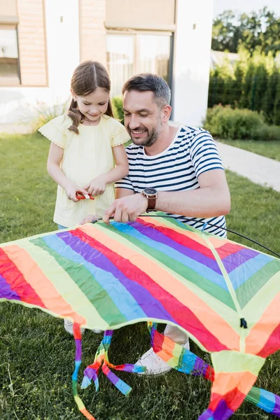 Volle Länge der lächelnden Tochter, die neben Vater steht, der Drachen auf Rasen montiert, mit verschwommenem Haus im Hintergrund — Stockfoto