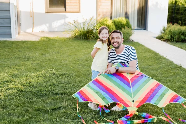 Glückliche Tochter und Vater mit Drachen schauen auf dem Rasen in die Kamera — Stockfoto