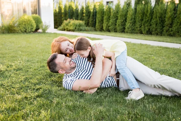 Щаслива сім'я сміється, лежачи на газоні на розмитому фоні — стокове фото