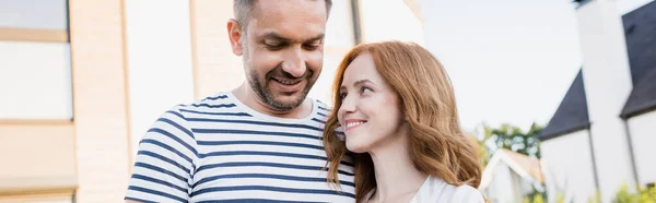 Femme rousse souriante regardant l'homme avec maison floue sur fond, bannière — Photo de stock