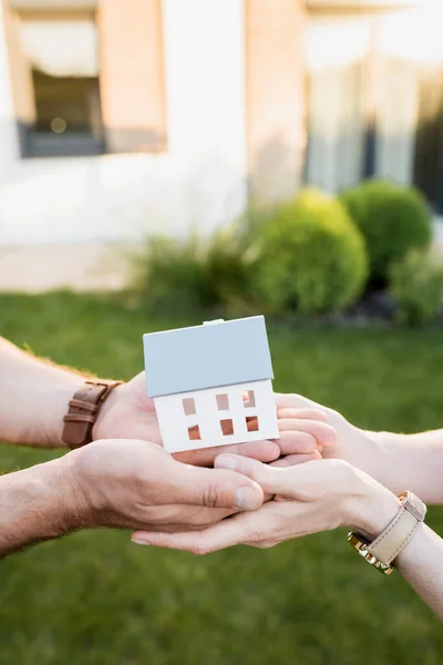 Vue recadrée de la statuette de la maison dans les mains du couple sur fond flou — Photo de stock