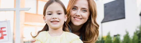 Retrato de la madre y la hija feliz mirando a la cámara sobre fondo borroso, pancarta - foto de stock