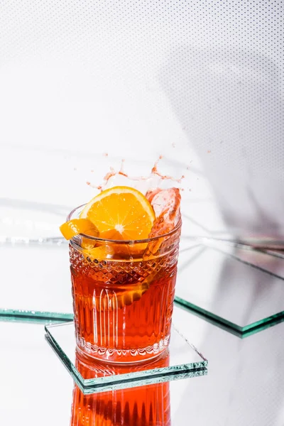 Cáscara de naranja en vidrio con cóctel de alcohol salpicado en blanco - foto de stock