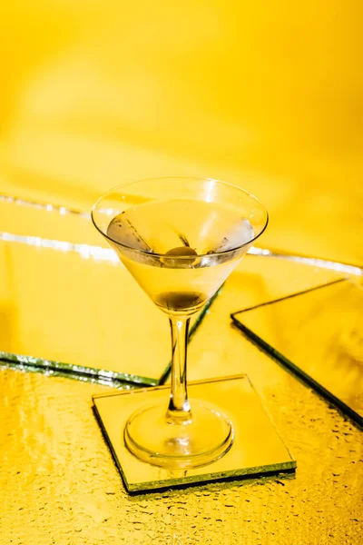 Green olive in glass of martini on yellow — Stock Photo