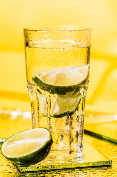 Limettenscheiben im Glas mit Rum auf gelb — Stockfoto