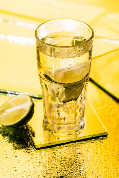 Lime en tranches dans un verre avec cocktail d'alcool sur jaune — Photo de stock