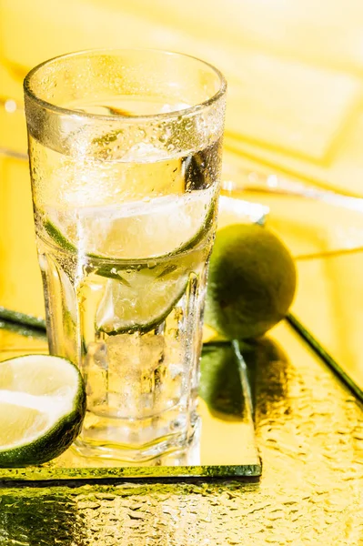 Glass of alcohol cocktail near sliced lime on yellow — Stock Photo