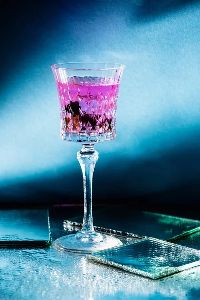 Purple cocktail in glass near mirrors on surface and blue background — Stock Photo