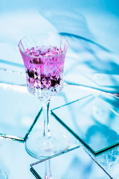 Cocktail de álcool roxo em vidro perto de espelhos na superfície e fundo azul — Fotografia de Stock