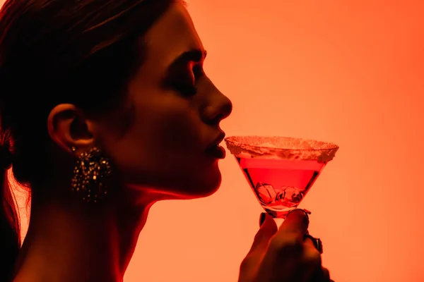 Vista laterale di giovane donna con gli occhi chiusi bere cocktail margarita su arancione — Foto stock