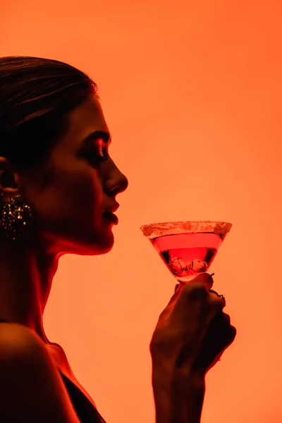 Vue latérale de la jeune femme tenant cocktail margarita sur orange — Photo de stock