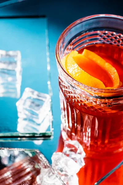 Cóctel de alcohol mezclado con whisky y naranja cerca de cubitos de hielo en azul - foto de stock