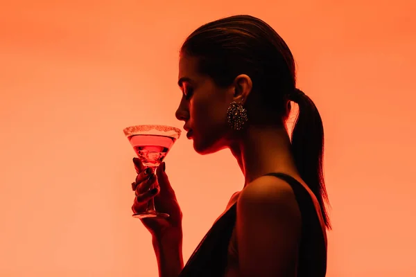 Side view of young woman holding margarita cocktail with ice cubes on orange — Stock Photo