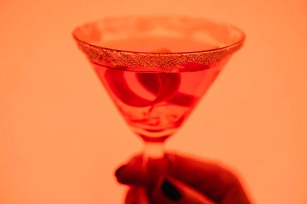 Close up of margarita cocktail with ice cubes and salt in female hand on orange — Stock Photo