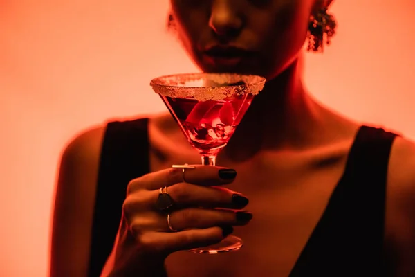 Margarita-Cocktail mit Eiswürfeln und Salz in der Hand einer Frau auf verschwommenem orangefarbenem Hintergrund — Stockfoto