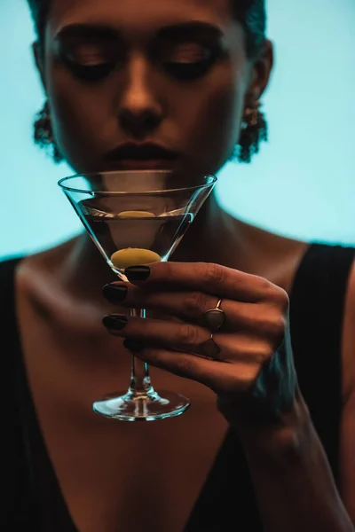 Glass of martini with olive in hand of woman on blurred background isolated on blue — Stock Photo