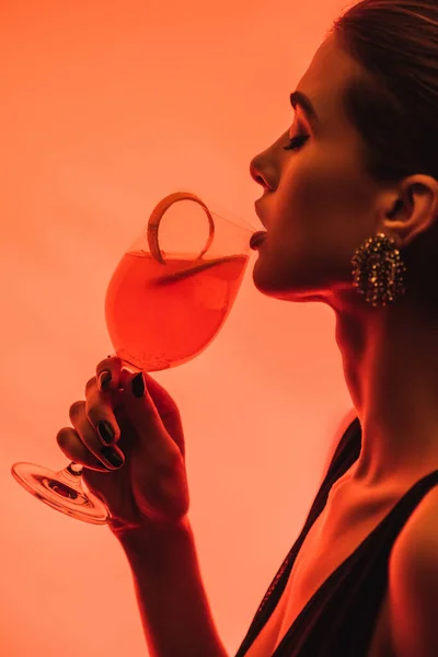 Perfil de mujer sosteniendo vidrio con cóctel mixto y cáscara de naranja en rosa - foto de stock