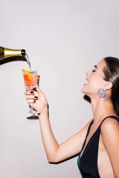 Champagne verser dans un verre avec cocktail de bouteille près femme heureuse sur blanc — Photo de stock