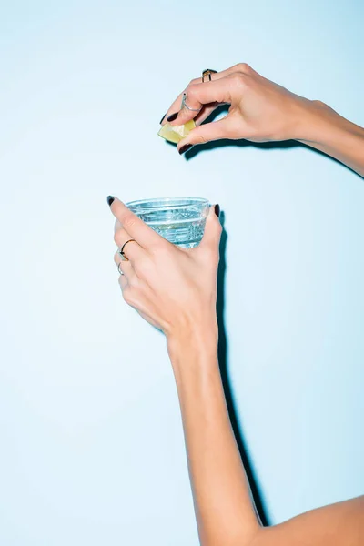 Cropped view of woman squeezing lime in glass with alcohol drink on blue — Stock Photo