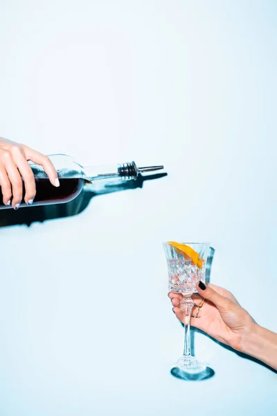 Vista recortada de la mujer sosteniendo botella cerca de vidrio con naranja en rodajas en azul - foto de stock