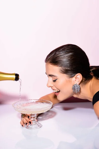 Mulher alegre olhando para champanhe em vidro perto de garrafa em branco — Fotografia de Stock