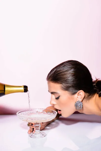 Mulher morena bebendo champanhe de vidro perto de garrafa em branco — Fotografia de Stock