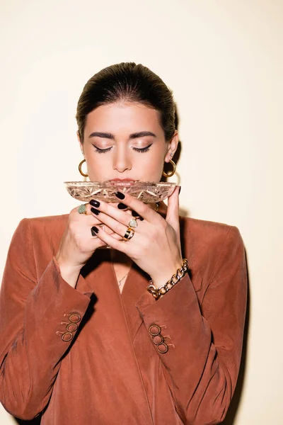 Brunette woman in brown blazer drinking champagne from glass on white — Stock Photo