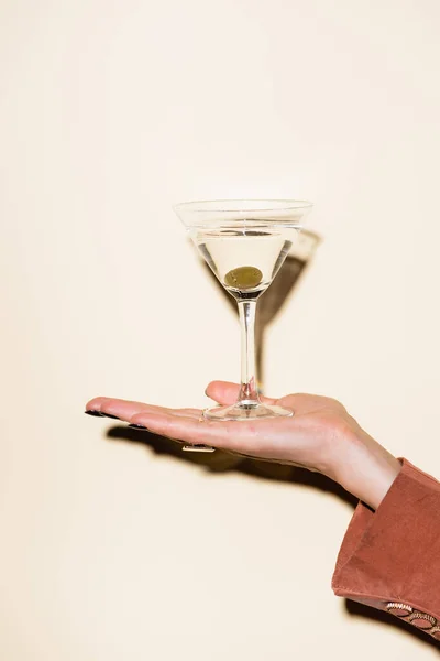 Cropped view of woman holding glass of martini with green olive in hand on white — Stock Photo