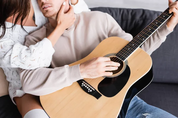 Обрезанный вид женщины, касающейся шеи парня с акустической гитарой на диване — стоковое фото