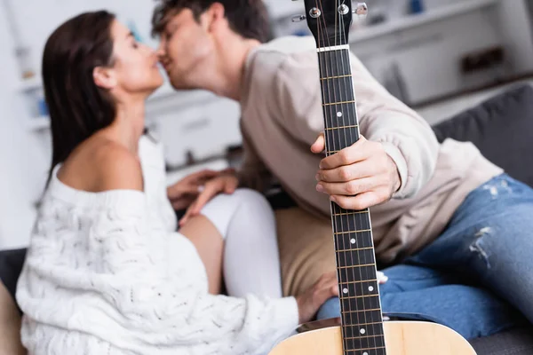 Acoustic guitar in hand of man kissing girlfriend on blurred background — Stock Photo