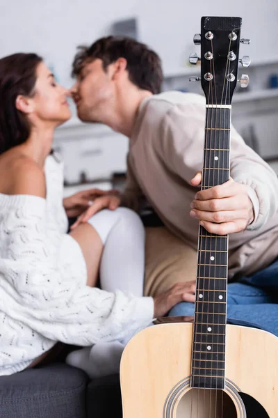 Guitare acoustique en main du jeune homme embrassant petite amie à la maison sur fond flou — Photo de stock