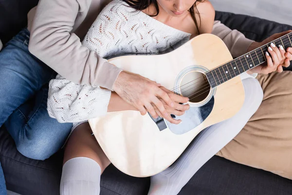 Обрезанный вид женщины, играющей на акустической гитаре с парнем на диване — стоковое фото