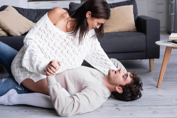 Jeune femme tenant la main du petit ami assis sur le sol à la maison — Photo de stock