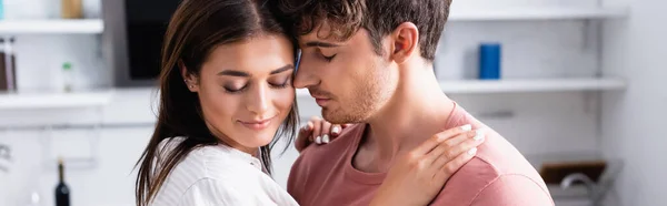 Mujer joven abrazando hombros de novio con los ojos cerrados en la cocina, pancarta - foto de stock