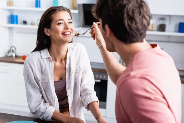 Lächelnde Frau schaut Freund an, der Waffel auf Gabel auf verschwommenem Vordergrund hält — Stockfoto