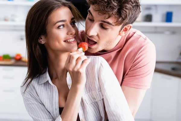 Smiling woman feeding boyfriend with fresh strawberry at home — Stock Photo