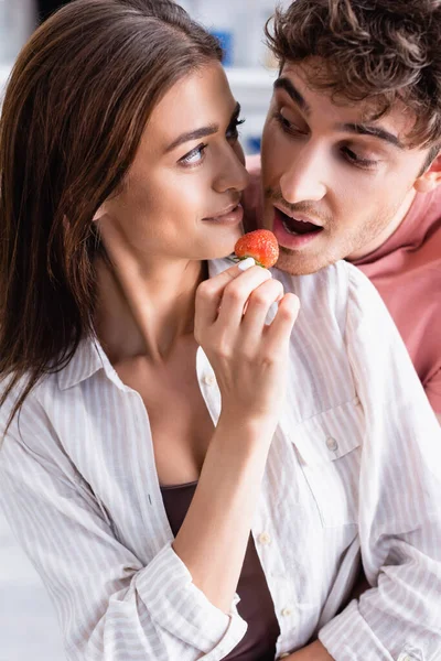 Mujer sonriente sosteniendo fresa cerca de novio en casa - foto de stock